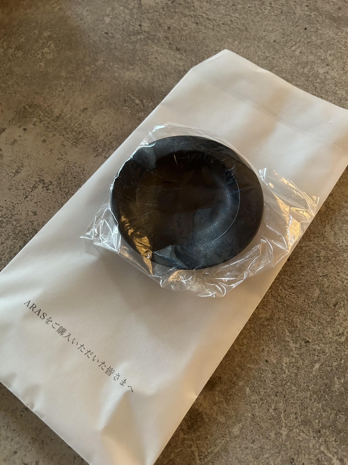 白い袋の上に置かれた包装済みのARAS黒い小皿、丁寧な梱包の様子