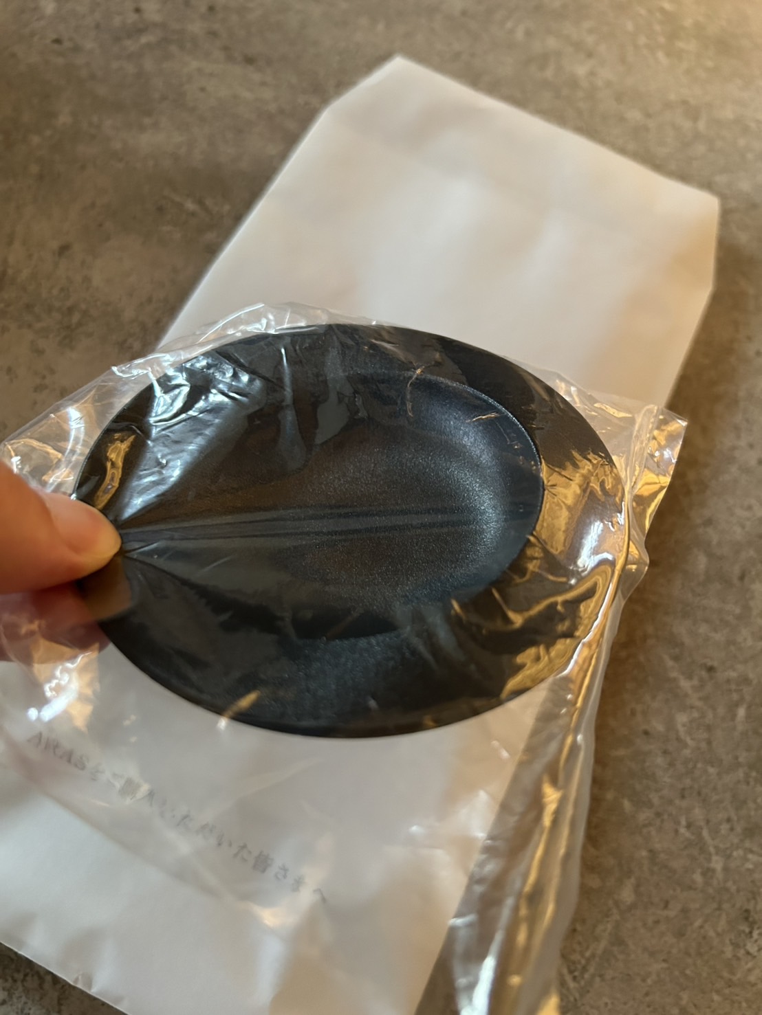 ビニール包装された黒い小皿を手に持つ開封シーン